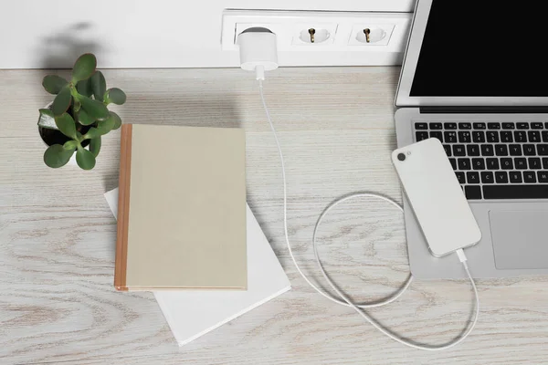Laptop ve akıllı telefon ahşap masada şarj oluyor.