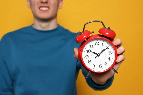 Young man with alarm clock on orange background, closeup. Being late concept