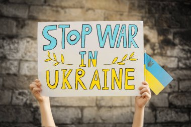 Ukrayna 'da Savaşı Durdurun posterini tutan çocuk ve tuğla duvara karşı ulusal bayrak, yakın plan