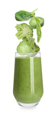 Taze sebzeler bardağa dökülüyor ve beyaz arka planda lezzetli meyve püresi var.