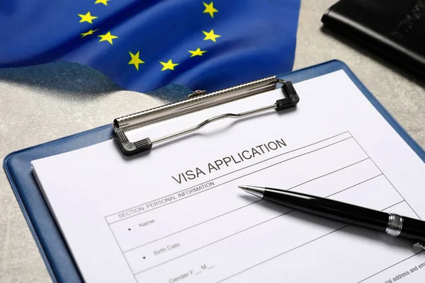 Visa application form, pen and flag of European Union on light grey table, closeup