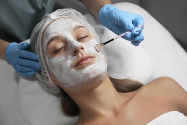 Spa salonu müşterinin yüzüne maske uygulayarak güzellik uzmanı