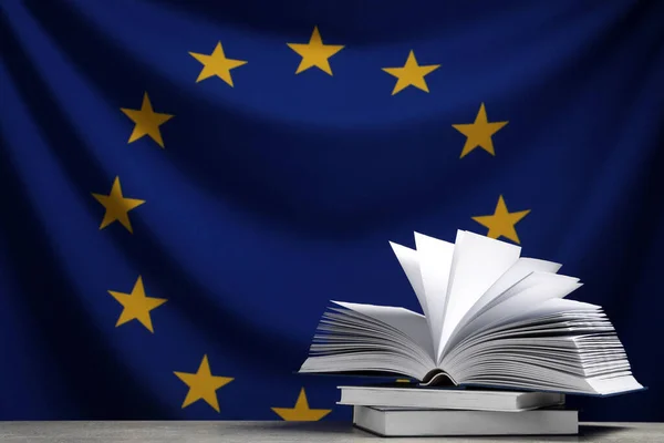 Books on light grey table against flag of European Union. Space for text