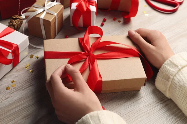 Woman decorating gift box at white wooden table, closeup. Christmas present