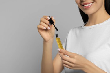 Açık gri arka planda kirpik yağı olan genç bir kadın, yakın plan. Metin için boşluk