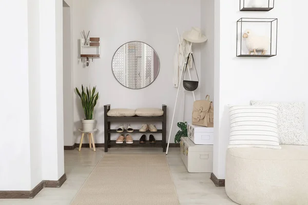 Hallway interior with stylish furniture and round mirror on light wall