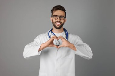 Doctor making heart with hands on grey background