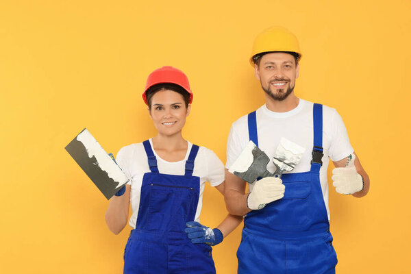 Professional workers with putty knives in hard hats on orange background