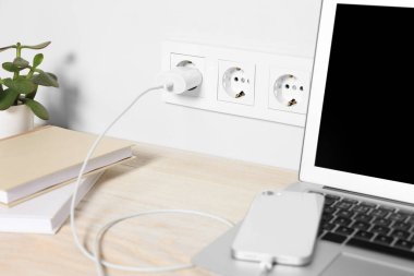 Laptop ve akıllı telefon ahşap masada şarj oluyor.