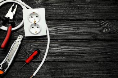 Elektrikçi aletleri ve elektrik prizi seti siyah ahşap masada, düz yerde. Metin için boşluk