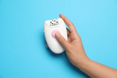 Açık mavi arka planda modern epilatör tutan kadın, üst görünüm