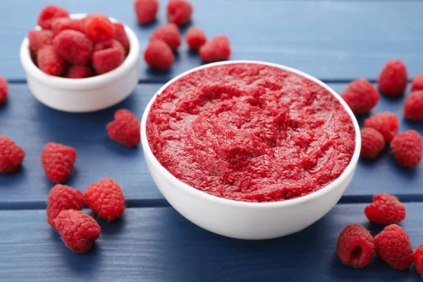 Raspberry puree in bowl and fresh berries on blue wooden table, closeup