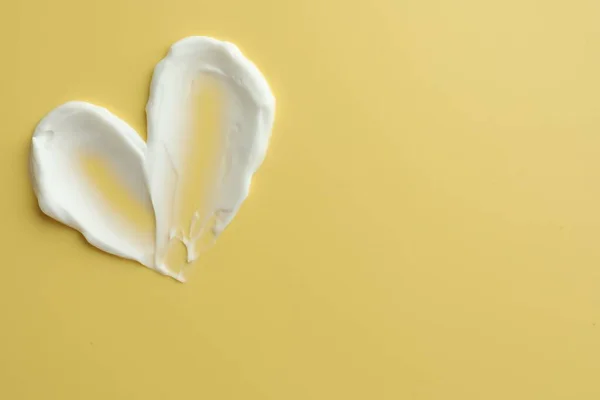 Samples of face cream in shape of heart on yellow background, top view. Space for text