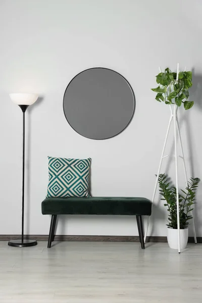 Stylish round mirror on white wall over bench in room
