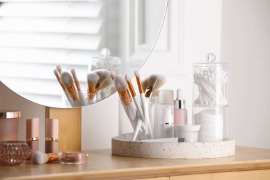 Containers with cotton swabs and pads near cosmetic products on dressing table