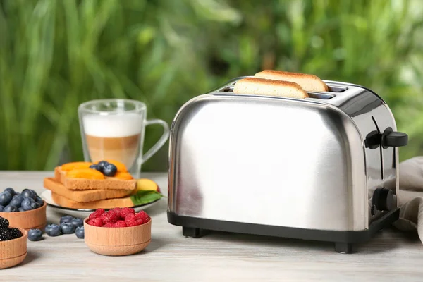 白色木制桌子上的现代烤面包机和新鲜产品 绿色背景模糊 — 图库照片