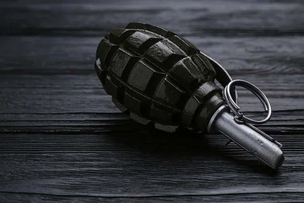 Hand grenade on black wooden table, closeup. Explosive weapon