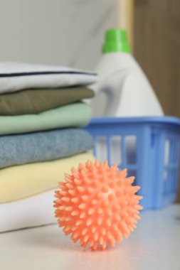 Beyaz masadaki turuncu kurutma makinesi temiz kıyafetlerin yanında, yakın plan.