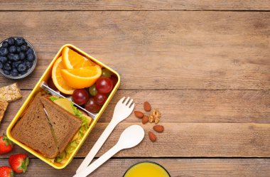 Beslenme çantalı düz kompozisyon ve ahşap masada lezzetli sağlıklı yiyecekler, mesaj için yer. Okul yemeği.