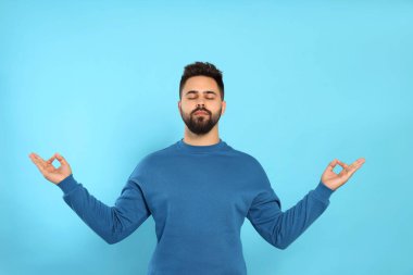Genç adam açık mavi arka plan üzerinde meditasyon yapıyor. Zen kavramı