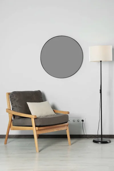 Stylish round mirror on white wall over armchair in room