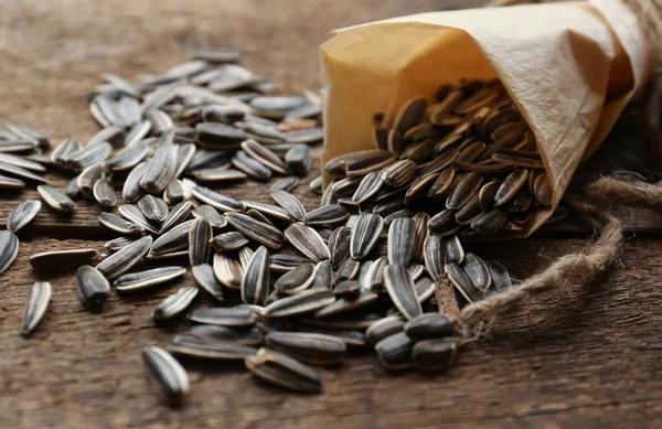 Overturned paper cone with sunflower seeds on wooden table, closeup