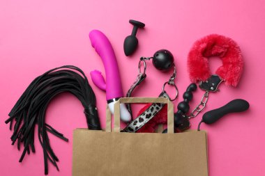 Pembe arka plan üzerinde farklı seks oyuncakları ile Kağıt alışveriş çantası, düz yatıyordu