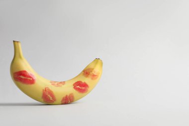 Banana covered with red lipstick marks on light grey background, space for text. Potency concept clipart