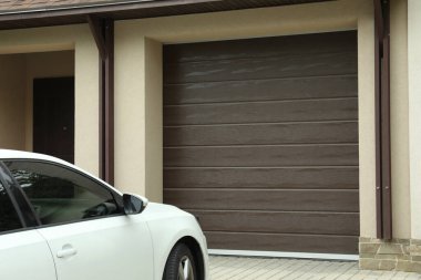Kahverengi bölümlü garaj kapısı ve park edilmiş arabası olan bir bina.