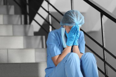 Yorgun doktor hastanede merdivenlerde oturuyor, mesaj için yer var.