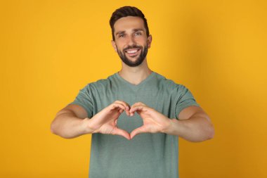 Happy man making heart with hands on yellow background