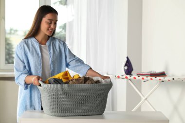 Young woman with basket full of clean laundry at table indoors