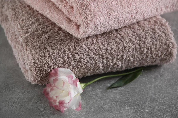 Folded soft towels with flower on grey table, closeup