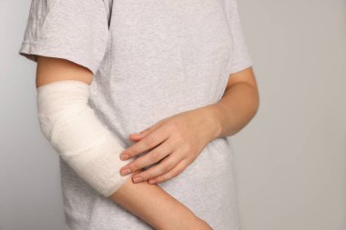 Kolu bandajlı bir kadın açık gri arka planda, yakın plan