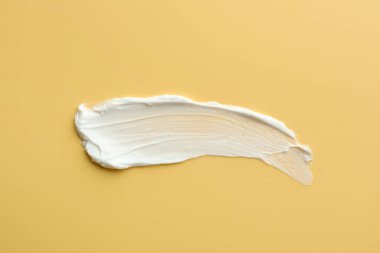 Sarı arka planda yüz kremi örneği, üst görünümde.