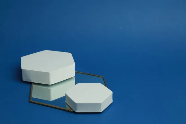 Product photography props. Hexagonal shaped podiums and mirror on blue background, space for text