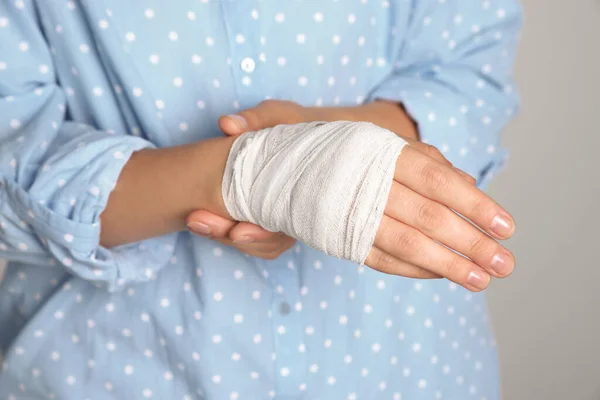 Woman with hand wrapped in medical bandage on light grey background, closeup