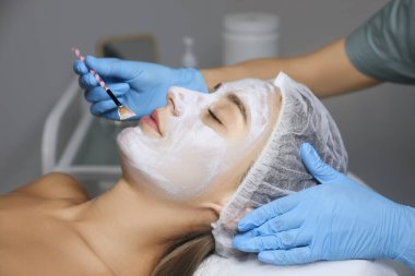 Spa salonu müşterinin yüzüne maske uygulayarak güzellik uzmanı