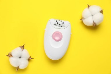 Sarı arka planda modern epilator ve pofuduk pamuk çiçekleri, düz yatıyordu