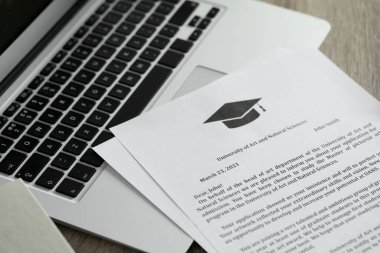 Üniversitelerden ve laptoptan kabul mektupları ahşap masa içinde, yakın plan.