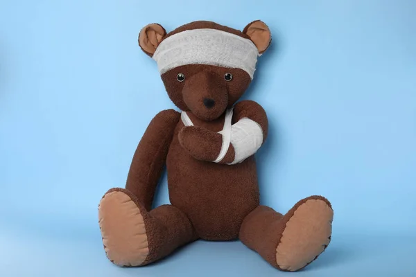 Toy bear with bandages on light blue background