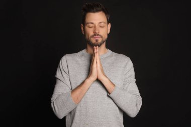 Elleri sıkıca bağlı siyah arka planda dua eden adam.