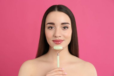 Pembe arka planda doğal yeşil yüz silindiri kullanan kadın.