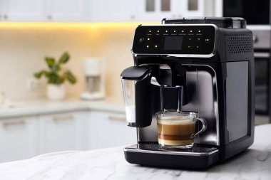 Modern kahve makinesi, mutfakta beyaz mermer tezgahın üzerinde cam bir fincan latte.