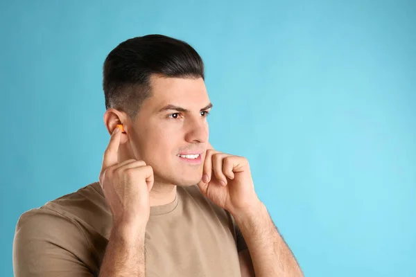 Man inserting foam ear plugs on light blue background. Space for text