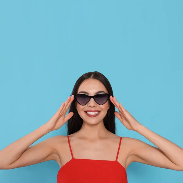 Aantrekkelijke Vrolijke Vrouw Aanraken Modieuze Zonnebril Tegen Licht Blauwe Achtergrond — Stockfoto