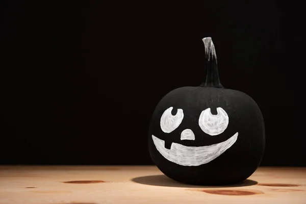 Halloween celebration. Pumpkin with drawn face on wooden table against black background, space for text