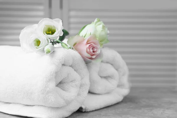 Rolled towels and flowers on grey table indoors