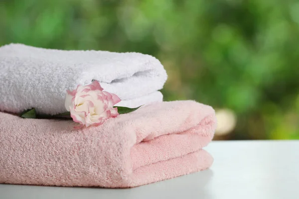 Folded towels with flower on white table against blurred background, space for text