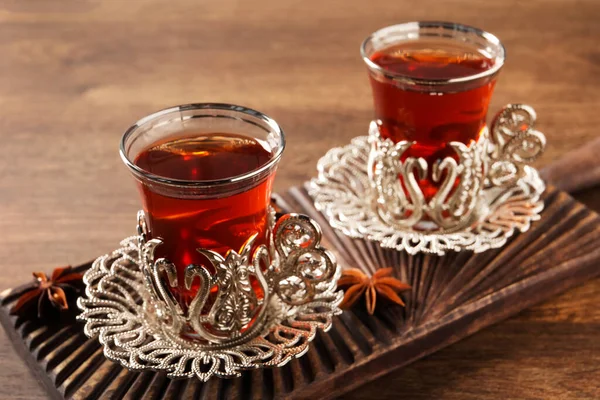 Glasses of traditional Turkish tea in vintage holders and anise stars on wooden table, closeup